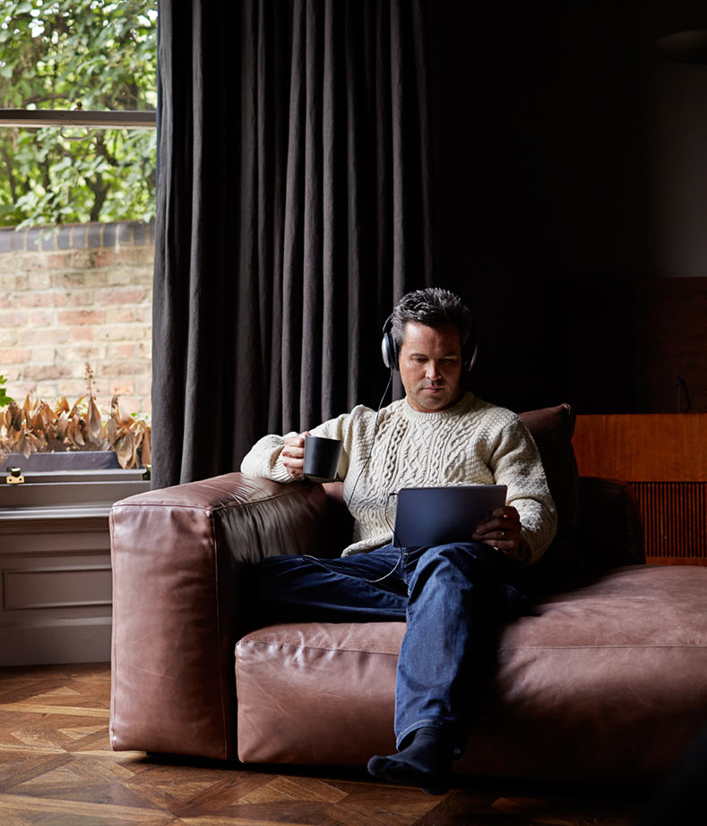 Mann entspannt auf Ledercouch mit Kopfhörern und Tablet im Hobbyraum